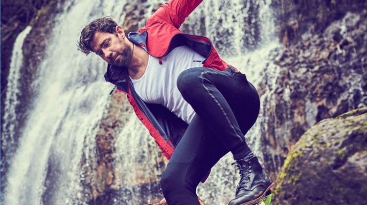 Actor John Krasinski wears a Z Zegna windbreaker, Calvin Klein tank, New Balance joggers, American Trench socks, a Breitling watch, and David Yurman necklace.