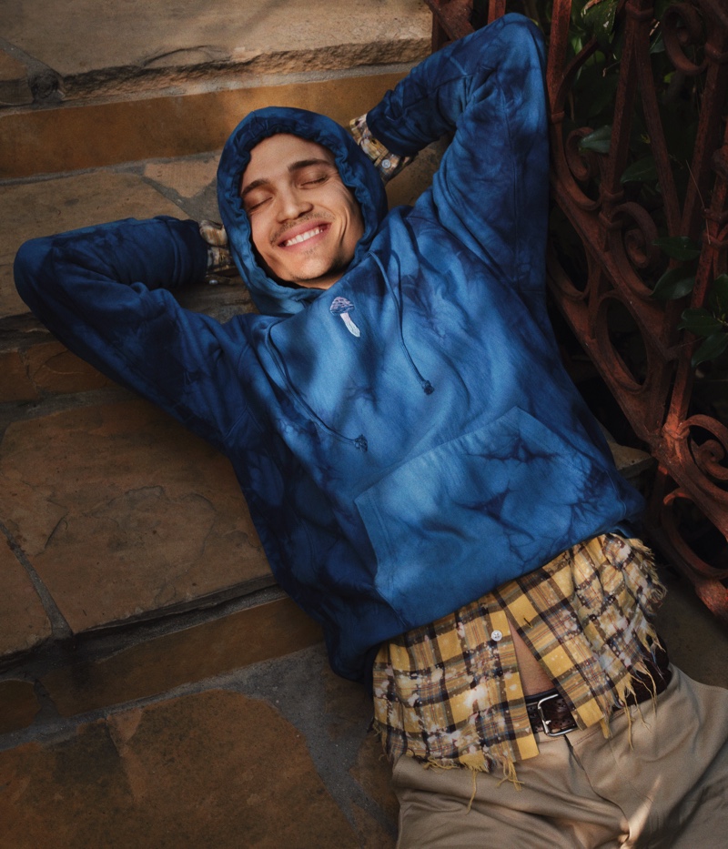 Linking up with Mr Porter, Karl Glusman relaxes in a tie-dyed hoodie by Story MFG. An AMIRI distressed flannel shirt, Chimala trousers, and a Sid Mashburn belt complete his look.