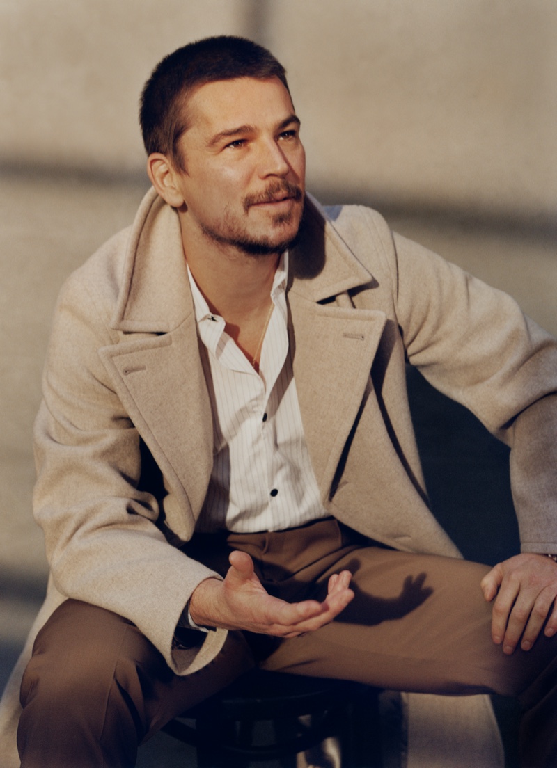 Sitting for a photo, Josh Hartnett sports an Auralee wool coat, Mr P shirt, and Brioni trousers.